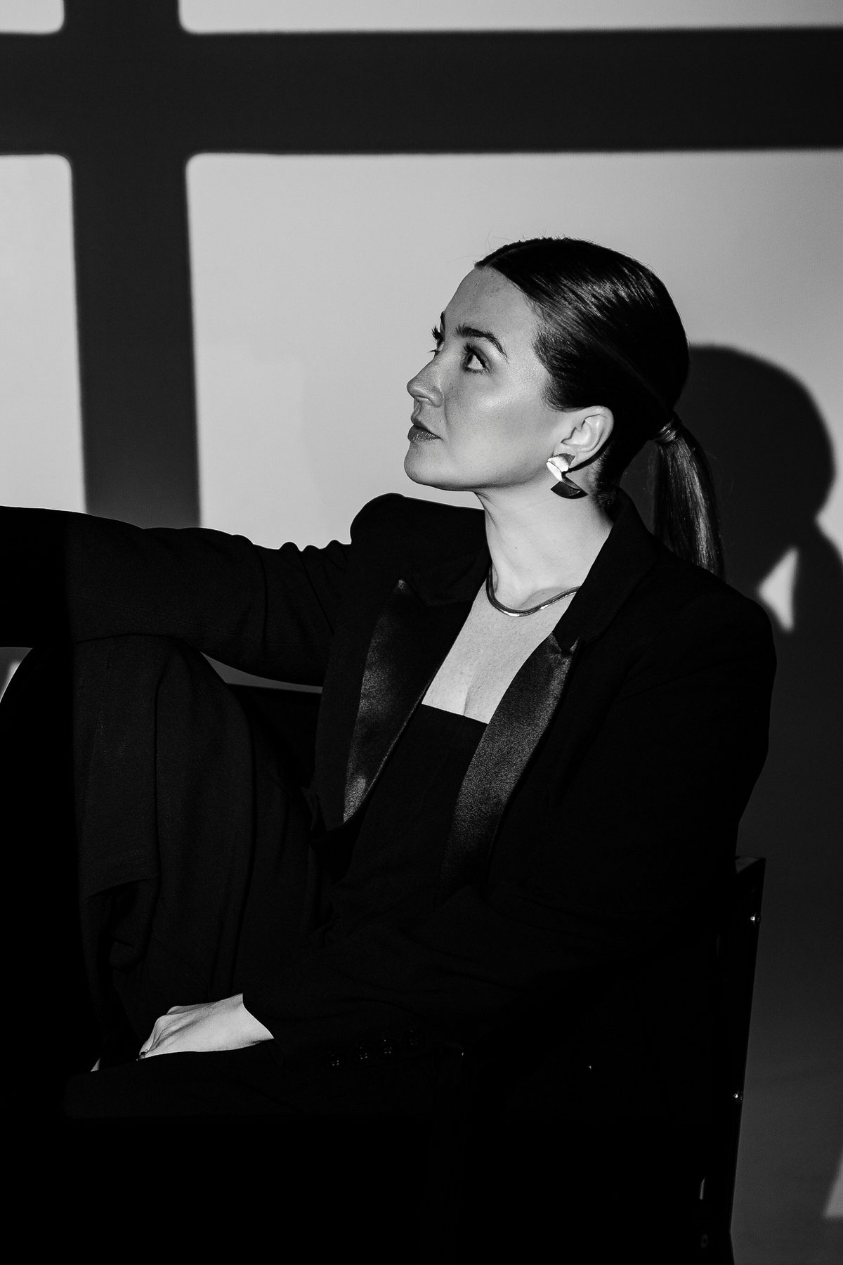 Retrato em preto e branco, mulher sentada de perfil com luz projetando sombra de janela